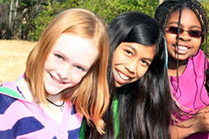 Three girls of different ethnicities pose together and smile for a photo.