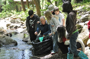 Adult holds a small net over the creek showing a group of children what she has caught.