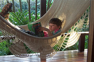 Young boy lounging in a hammock reading a book