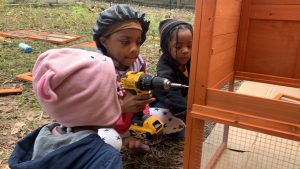 Three chidlren use a power drill to help assemble a chicken Coop. 