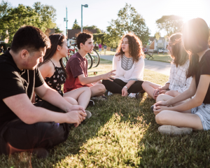 teens sitting in a circle in the grass talking with sun in the background